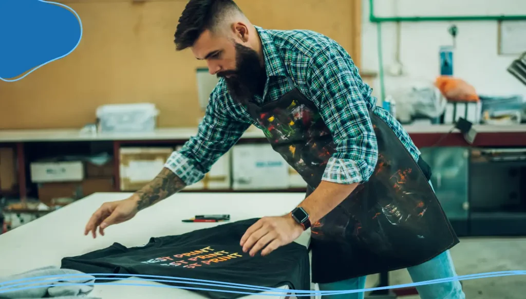 Male worker folding a fresh printed t shirt in a printing workshop.