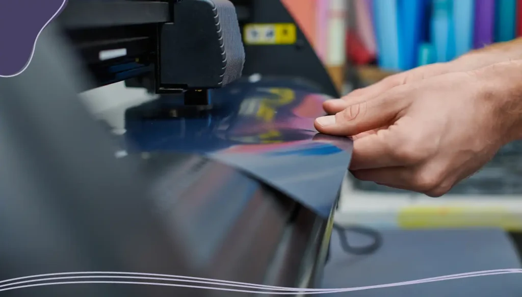 Cropped view of young craftsman holding layer near screen printing machine in blurred workshop.